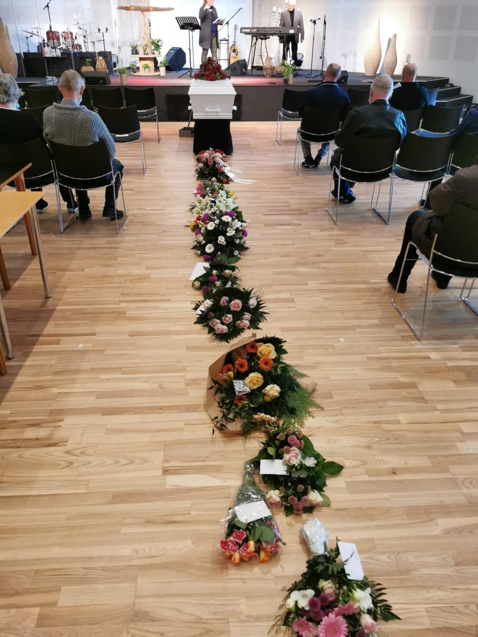En hvid kiste med røde roser står foran scenen i kirkesalen