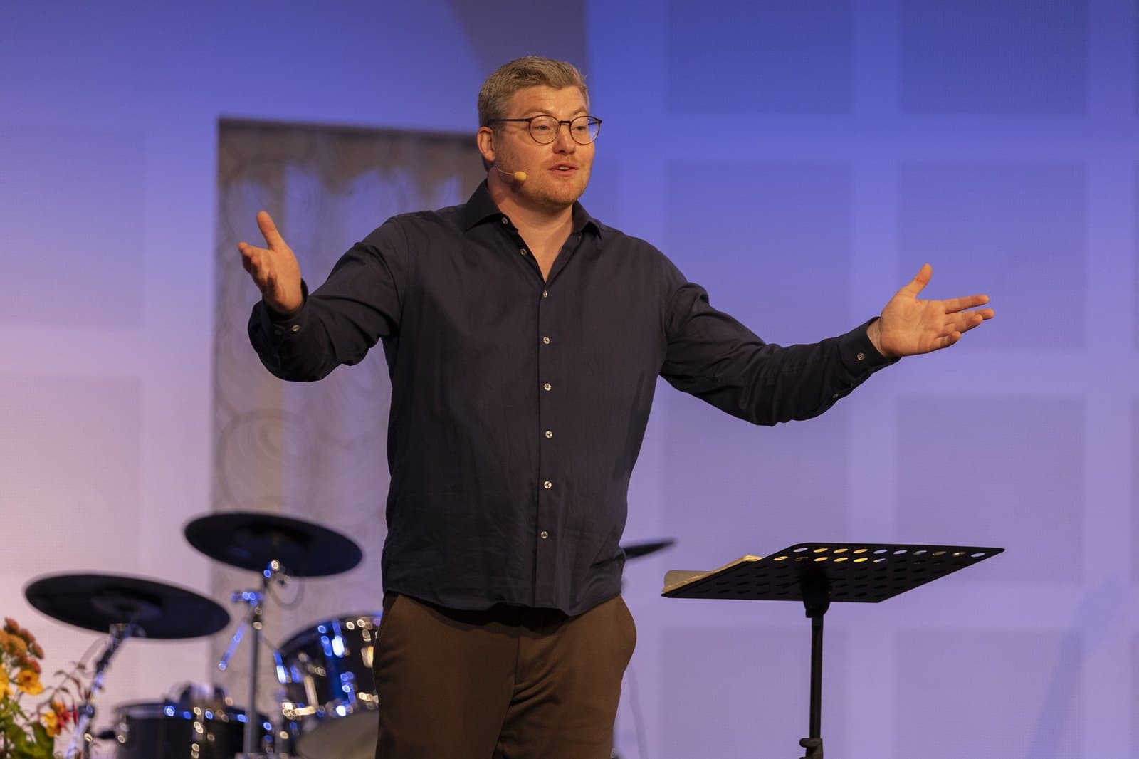 Sebastian Fredegod, præst i Kirken ACTS Vejle, taler med udbredte arme på scenen
